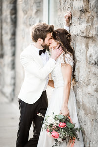 Groom kisses his bride against stone wall