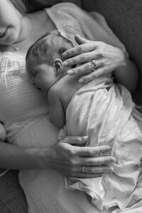 Mother holds her newborn baby on her chest during a newborn session at home.