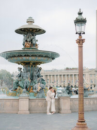 a man and woman standing in front of a large fountain facing each other
