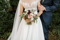 bride carrying a bouquet in white, blush, burgundy, and greenery