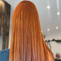 Straight, vibrant copper-red hair with sleek texture, photographed under salon lighting.
