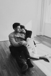 Couple sits on floor cuddling and leaning on each other