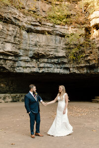 Couple holding hands and talking to one another next to a cave.