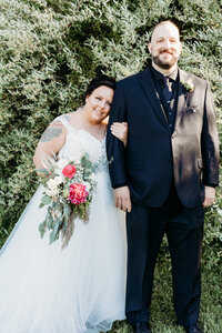 A bride hangs on the arm of her tall groom's arm outdoors