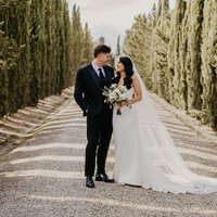 Coppia di sposi che si guarda negli occhi in un vialetto di cipressi presso Borgo Divino.