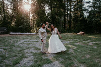 Groom twirling his bride in a forest clearing during golden hour, surrounded by tall pine trees and soft evening light.