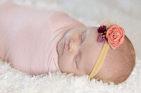 A newborn baby girl wrapped in bed sleeping on a fuzzy white blanket.