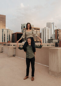 Girl sitting on her fiancee's shoulders on a city rooftop