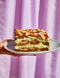 hand holding a plate of green tiramisu  in front of a purple curtain