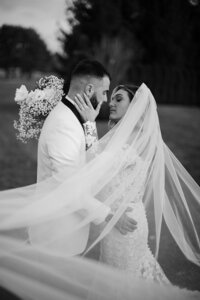 The bride and groom share a tender embrace, locking eyes and reaching in for a kiss, while the bride's veil gracefully unfolds.