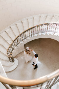 Photo of bride ad groom standing at bottom of curving staircase while groom twirls bride taken by Intimate wedding photographer Portland Maine