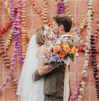Newlyweds kissing in front of a garland of flowers