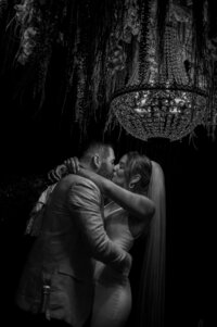 Romantic black and white wedding photo of a couple sharing a kiss beneath a crystal chandelier during an intimate moment at Cederville Lodge.