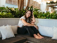 woman sitting on a couch in black ripped jeans smiling with her head resting on her hand
