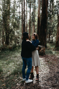 engaged couple share and intimate moment together in the forest hugging and laughing