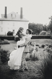 Groom lifting bride in the garden outside a historic estate during their Portland Maine wedding, captured in black and white.