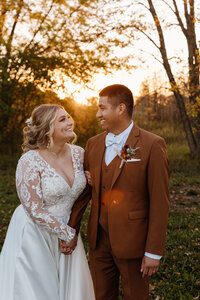 A newlywed couple holding hands and smiling at sunset