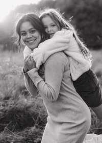 a black and white photo of a mom and her daughter hugging her with her arms wrapped around her neck.