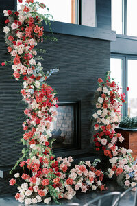 Indoor wedding floral installation with pink, red, and peach roses framing a modern fireplace for a luxury wedding at the Kimpton Armory.
