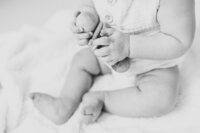 Black and white image of baby hands holding wooden rattle during baby photo session