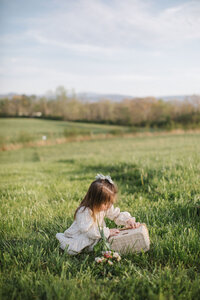 little girls picks fresh flowers in the middle of an open field in spring
