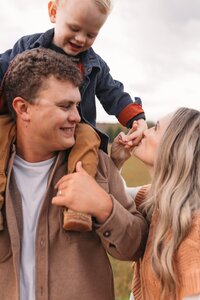 mom kissing her son's hand while he sits on his dad's shoulders