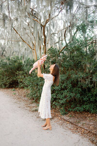 Mom holds up her daughter and smiles by spanish moss