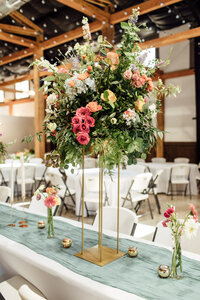 Table lined with a blue runner and. gold vases sitting on top with large florals on top