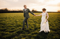Bride and Groom holding hands and walking through a field.