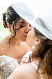 lesbian brides kissing with one of the bride's veils over their heads