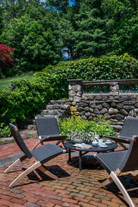 Historic home decorator in Boston created a modern outdoor space at a classic Boston estate with an original garden wall, climbing greens, and foldable furniture on aged brick.