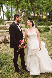 Bride smiling at groom holding colorful bouquet outdoors