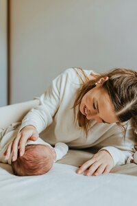 A newborn baby lays on a bed and a woman smiles and comforts them.