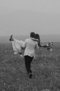 groom carrying bride through a field