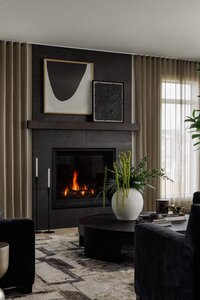 Elegant living room featuring a cozy fireplace, statement abstract artwork, taupe area rug, and tailored custom drapery for a warm, sophisticated ambiance.