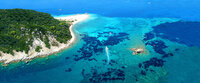 Aerial view of a tropical island with lush green vegetation, white sandy beaches, and clear turquoise waters with dark coral patches.