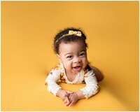 Child laying on mustard backdrop looking at camera and smiling
