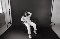 Sara Dobbins wearing all white leans back in chair in front of dark photo backdrop