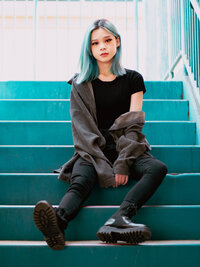 Portrait of creative woman with blue hair sitting on teal stairs, showcasing bold, edgy streetwear style – photographed by Mewphotovideo in Portland, Oregon.