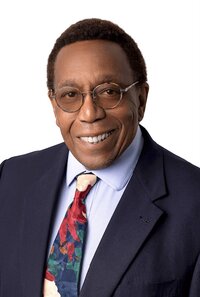 black mean in a suit wearing glasses smiling at the camera for a headshot