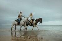 couple holds hands while riding horses on the beach in south florida