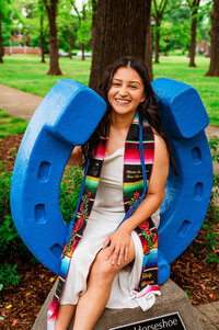 Senior girl sitting on the MTSU blue horseshoe wearing custom stole and cord