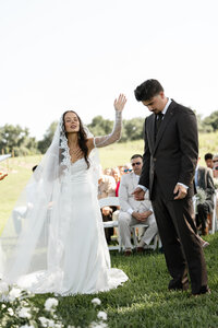 Bride in her veil and dress and sunglasses posing for her husband recording her on super 8 film.