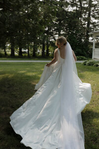 A bride running away from the camera, looking back and smiling during her portraits. The image is using motion blur to document the carefree nature of the bride. Captured by a Minnesota Wedding Photographer specializing in intimate, documentary style weddings.