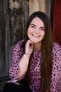 A Littleton senior photographer captures a senior girl in a pink leopard shirt holding her hand near her neck and smiling at the camera.
