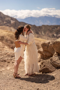 wo brides exchanging heartfelt vows in the vast desert landscape of Death Valley National Park, with golden sand dunes in the background