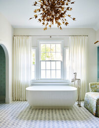Boston kitchen and bath designer created a custom primary bathroom with a gilded light fixture, freestanding tub, and linen embroidered drapery panels.