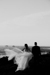 Bride and groom looking at the ocean. flowy wedding dress in wind