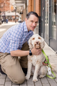Kelly's partner holds a dog while kneeling on the sidewalk