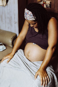 Birth photography in Tifton: woman focusing during contraction, sitting down, eyes closed, pregnant belly exposed